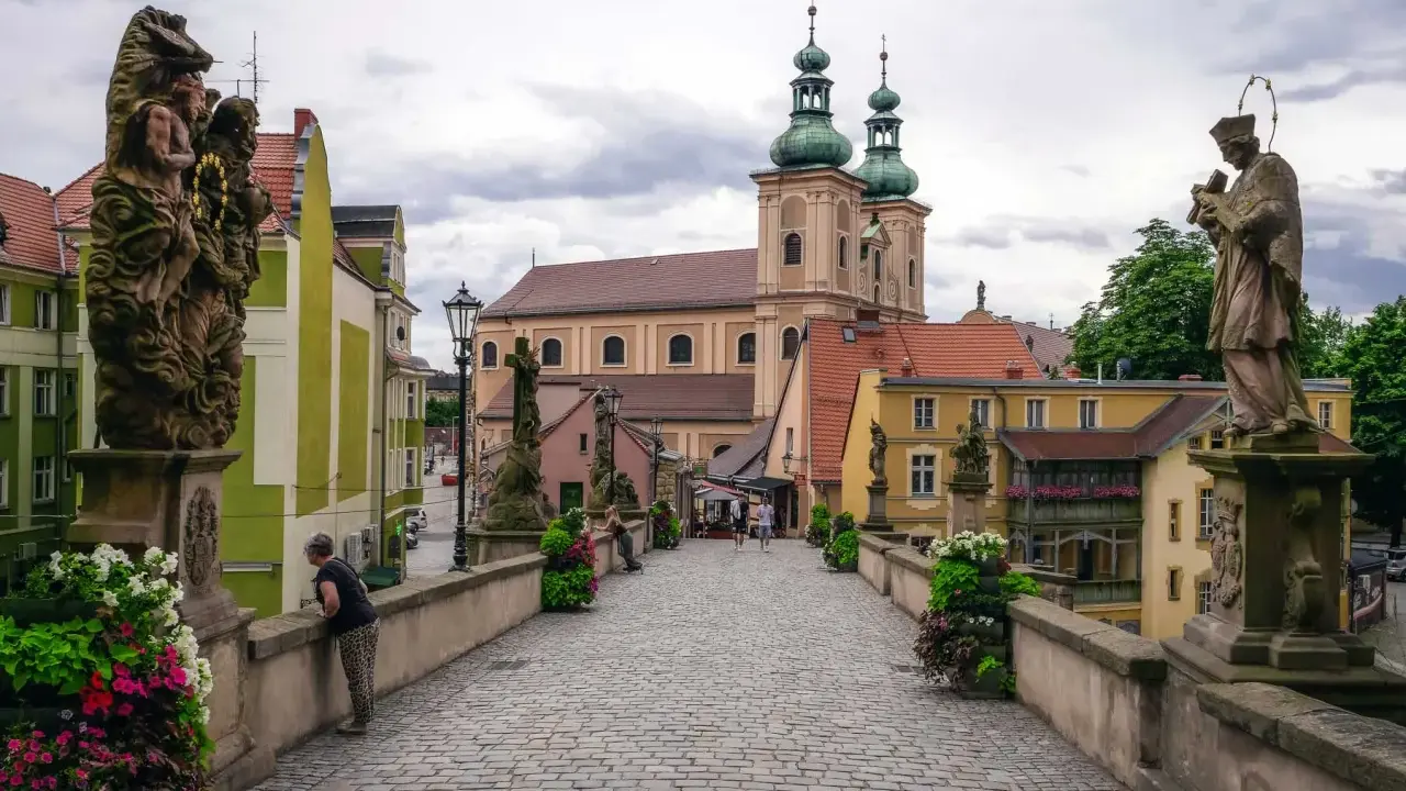 Kamienny most z rzeźbami i barokową architekturą, w tym kościołem z zielonymi kopułami. To piękne ziemia kłodzka atrakcje.