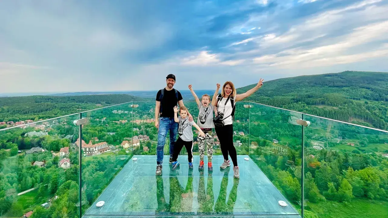 Rodzina cieszy się spacerem w chmurach w Szklarskiej Porębie. Szklany taras widokowy oferuje zapierający dech w piersiach widok na zielone wzgórza i miasteczko.