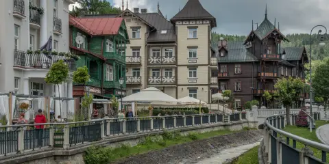 Krynica-Zdrój latem: malowniczy deptak nad potokiem, urokliwe kamienice i kawiarniane ogródki.