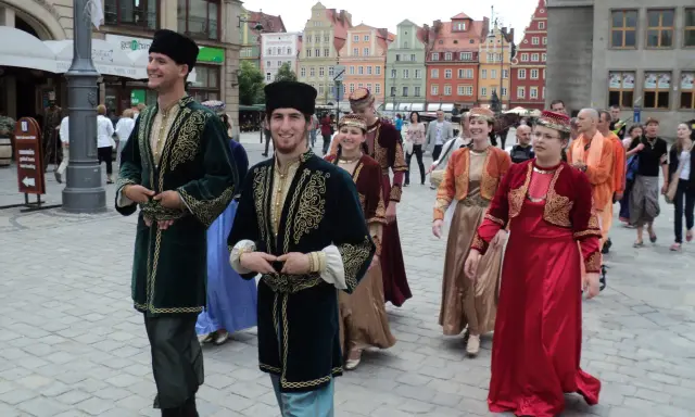 Ludzie w tradycyjnych strojach, wśród nich mężczyzna w zielonej kaftanie. Ciekawe karaimi ciekawostki w barwnym otoczeniu.