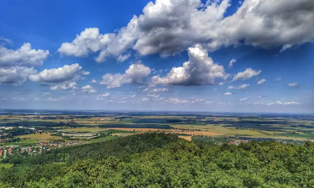 Widok z góry na pola, lasy i miasteczko. W oddali jezioro i błękitne niebo z chmurami. Ślęża atrakcje zapraszają do podziwiania krajobrazów.