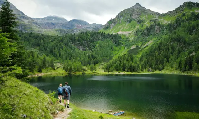 Para idąca ścieżką nad malowniczym jeziorem w Tatrach. W tle góry i lasy.