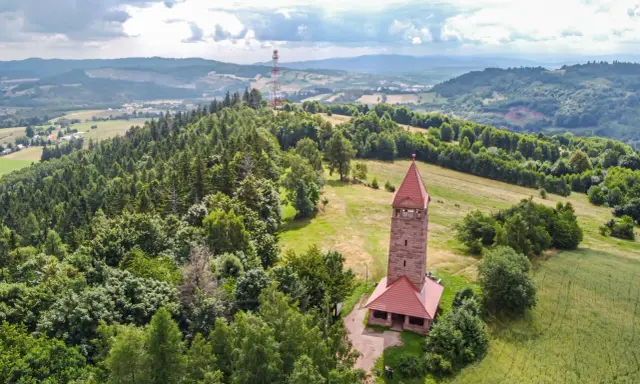 Kamienna wieża widokowa na wzgórzu, otoczona lasami i polami. Jedna z wielu wież widokowych na Dolnym Śląsku, oferująca piękne krajobrazy.