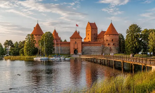 Zamek w Trokach, jedna z głównych atrakcji Litwy, z łodziami przy brzegu i drewnianym mostem.
