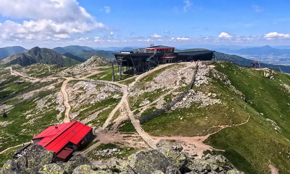 Widok na Chopok latem. Góry pokryte zielenią, kamieniste szlaki i nowoczesne budynki górnej stacji kolejki.