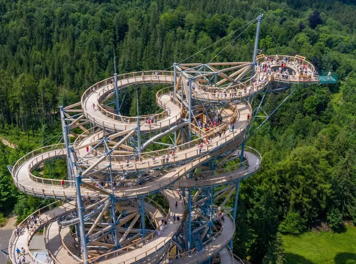 Drewniana konstrukcja wznosi się ponad lasem, oferując niezwykły spacer w chmurach w Szklarskiej Porębie. Ludzie przechadzają się po krętych ścieżkach, podziwiając widoki.