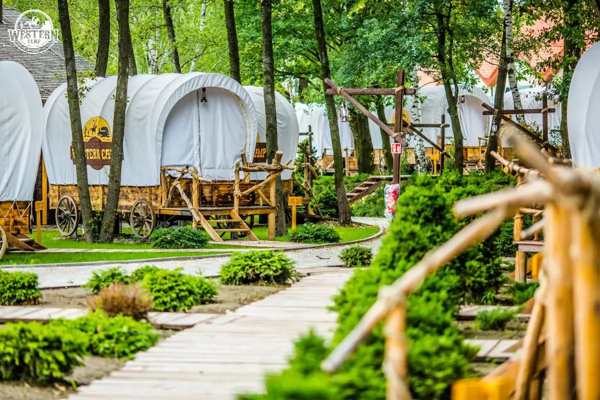 Kraków z dziećmi: drewniane wozy kempingowe w stylu western, otoczone zielenią, tworzą niezwykłą scenerię dla rodzinnej przygody.