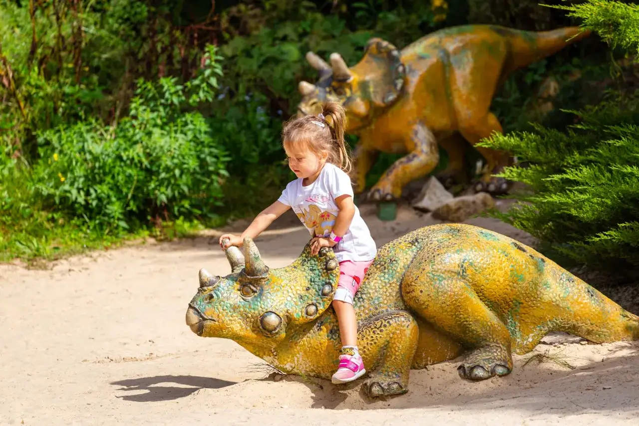 Mała dziewczynka siedzi na dinozaurze, odkrywając fajne miejsca w świętokrzyskim na weekend.